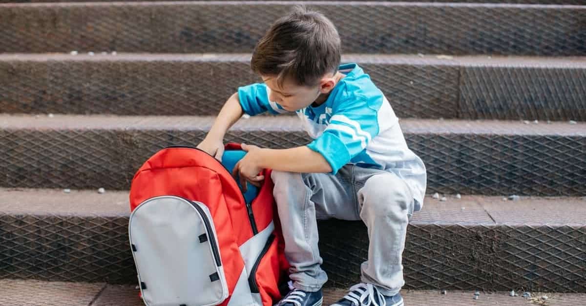 Young school boy reaches into a filled backpack