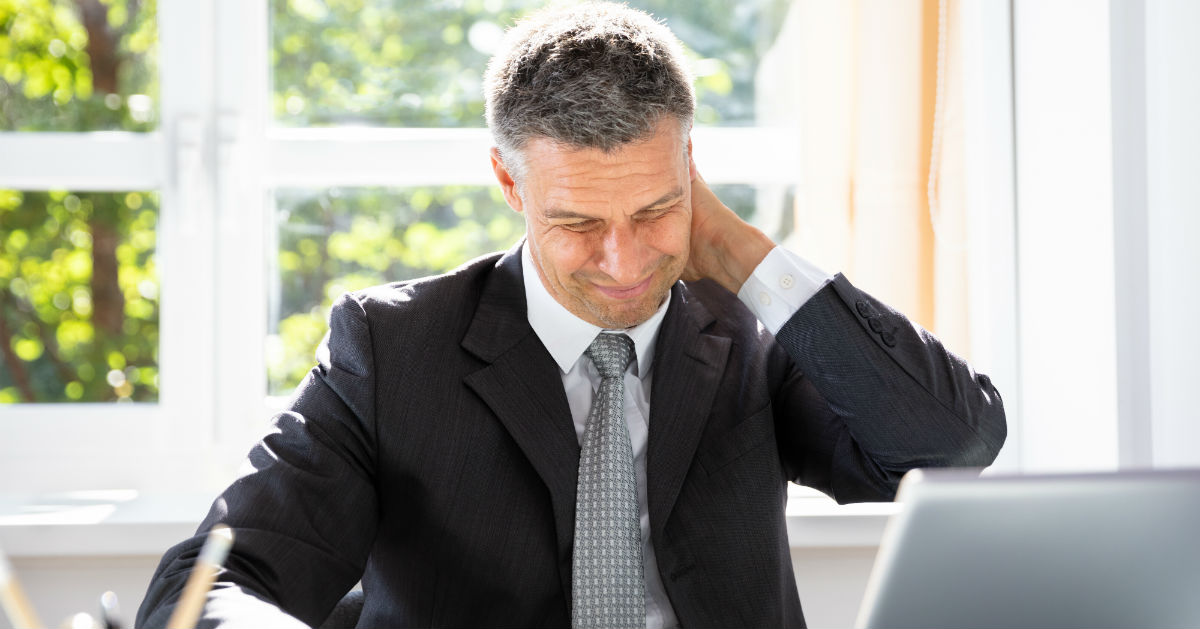 Man sitting at desk rubbing the back of his neck