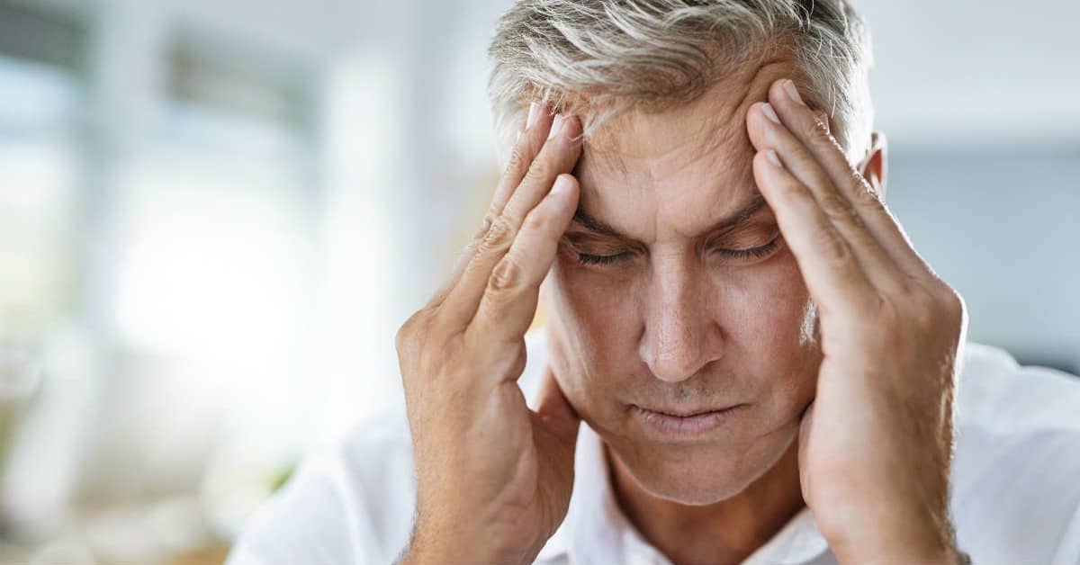 Man with hands on head; experiencing headache